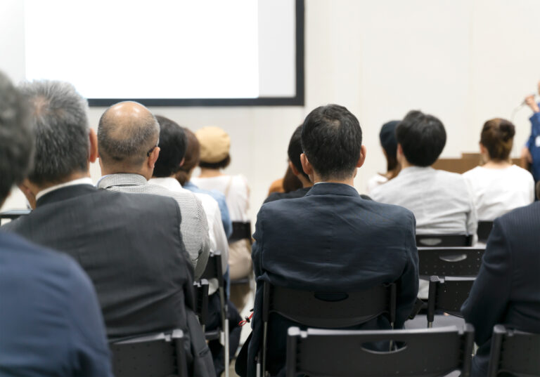 Audience members seated in chairs, attentively listening to a speaker at a seminar or presentation