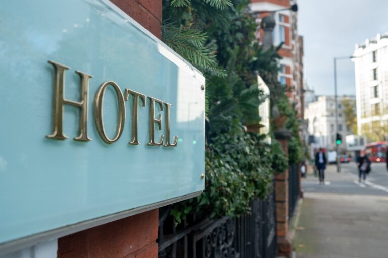 Elegant hotel sign on a city street, surrounded by greenery, with a mix of classic and modern architecture in the urban background.